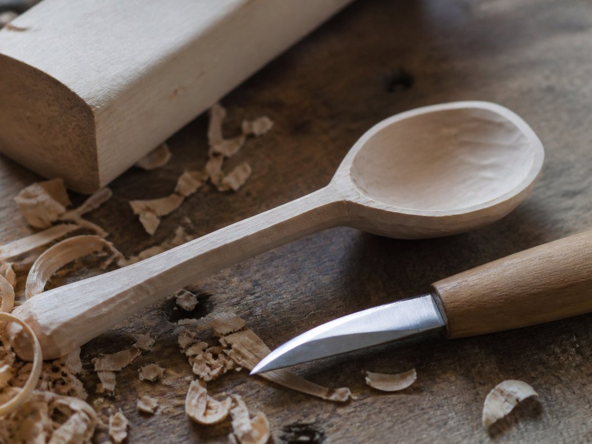 Wooden spoon being carved with shavings on a bench